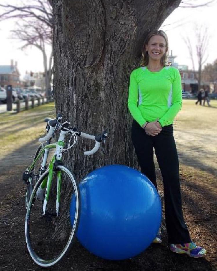 Kelley Dole leaning on a tree beside her bike and an exercise ball